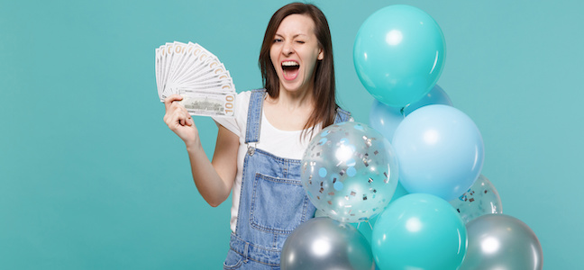 Funny blinking girl hold fan of money in dollar banknotes cash money celebrating with colorful air balloons isolated on blue turquoise wall background. Birthday holiday party, people emotions concept